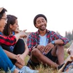 Smiling young people sitting and talking near bonfire